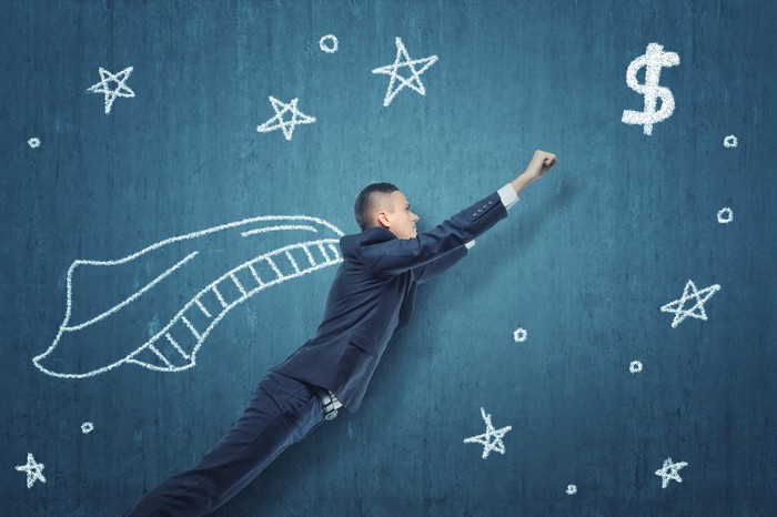 A man in a suit and an illustrated cape poses as if flying through space towards a dollar sign.
