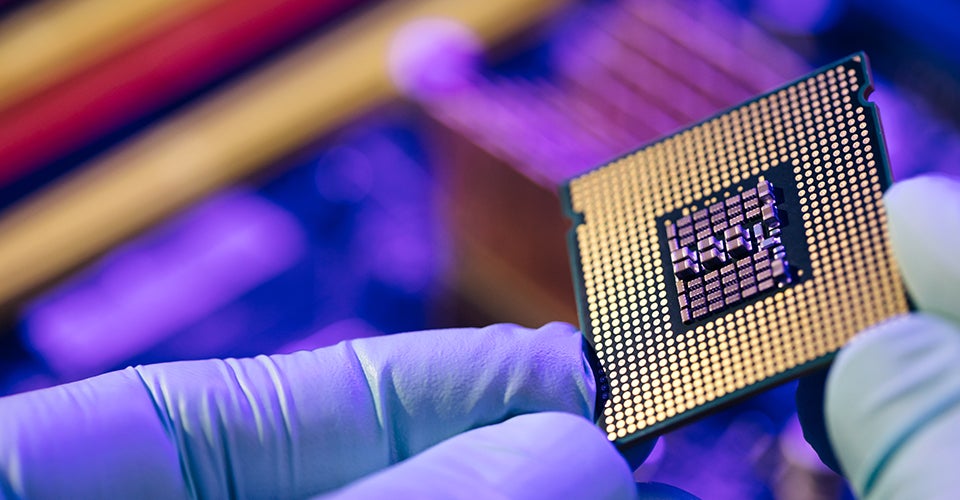 A worker holds a semiconductor chip up for inspection before adding it to a computer processor.